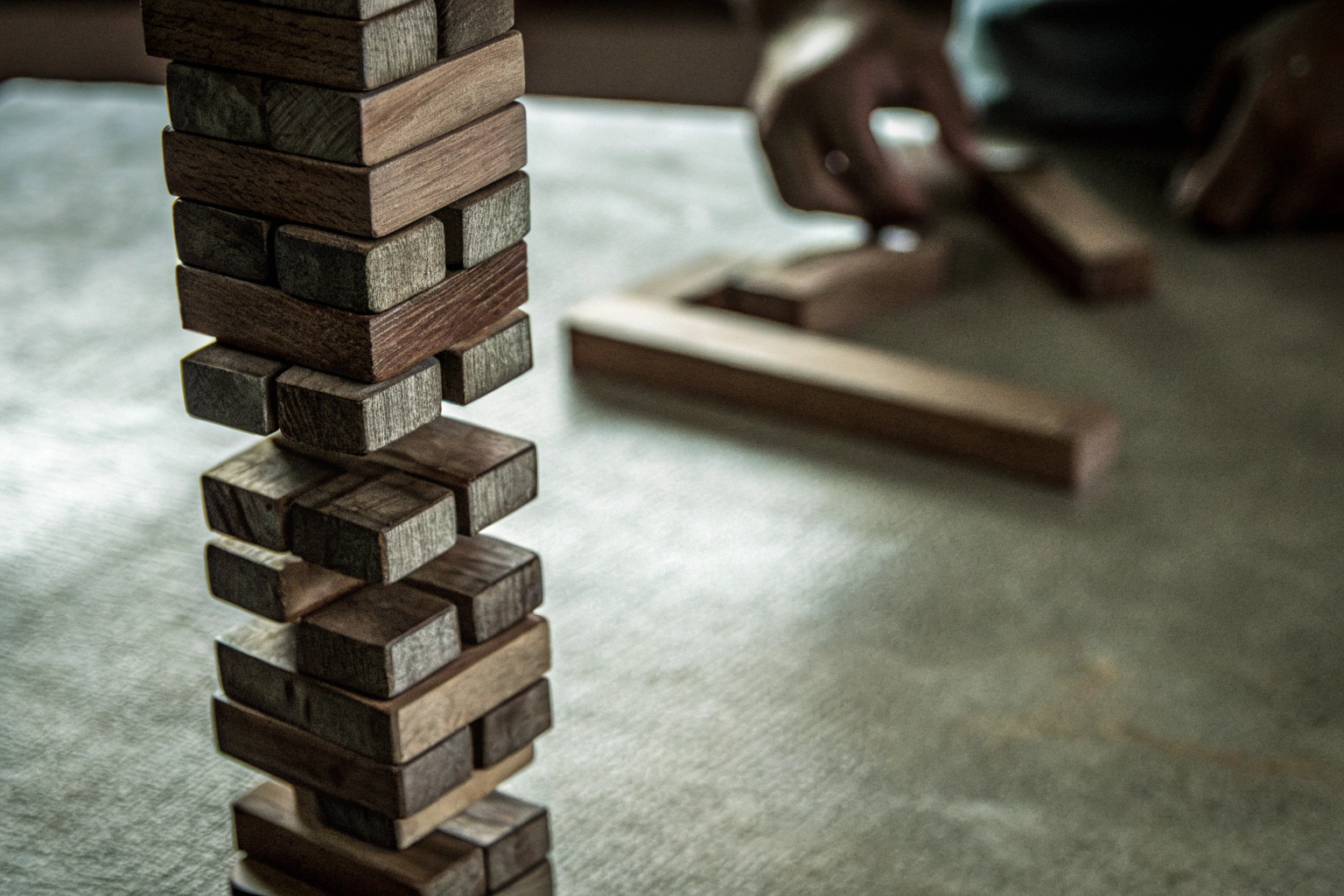 Detailaufnahme eines Jenga-Spiels in Aktion, bei dem ein Spieler einen Block herauszieht. Jenga-Spiel in Aktion