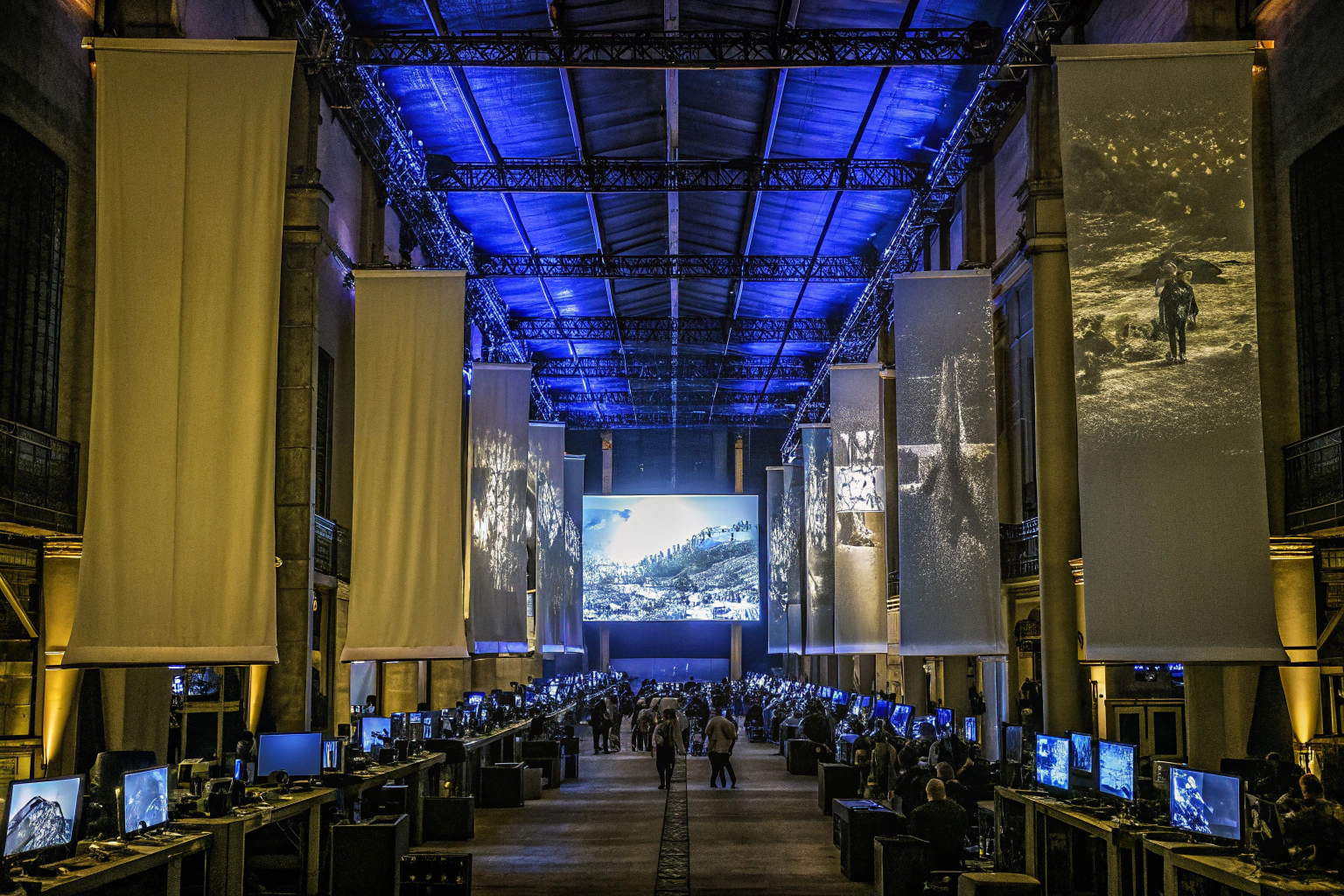 Ein Bild von einem aufregenden Gaming-Event mit vielen Besuchern und großen Bildschirmen, auf denen Spiele gezeigt werden. Gaming-Event mit vielen Menschen und Bildschirmen