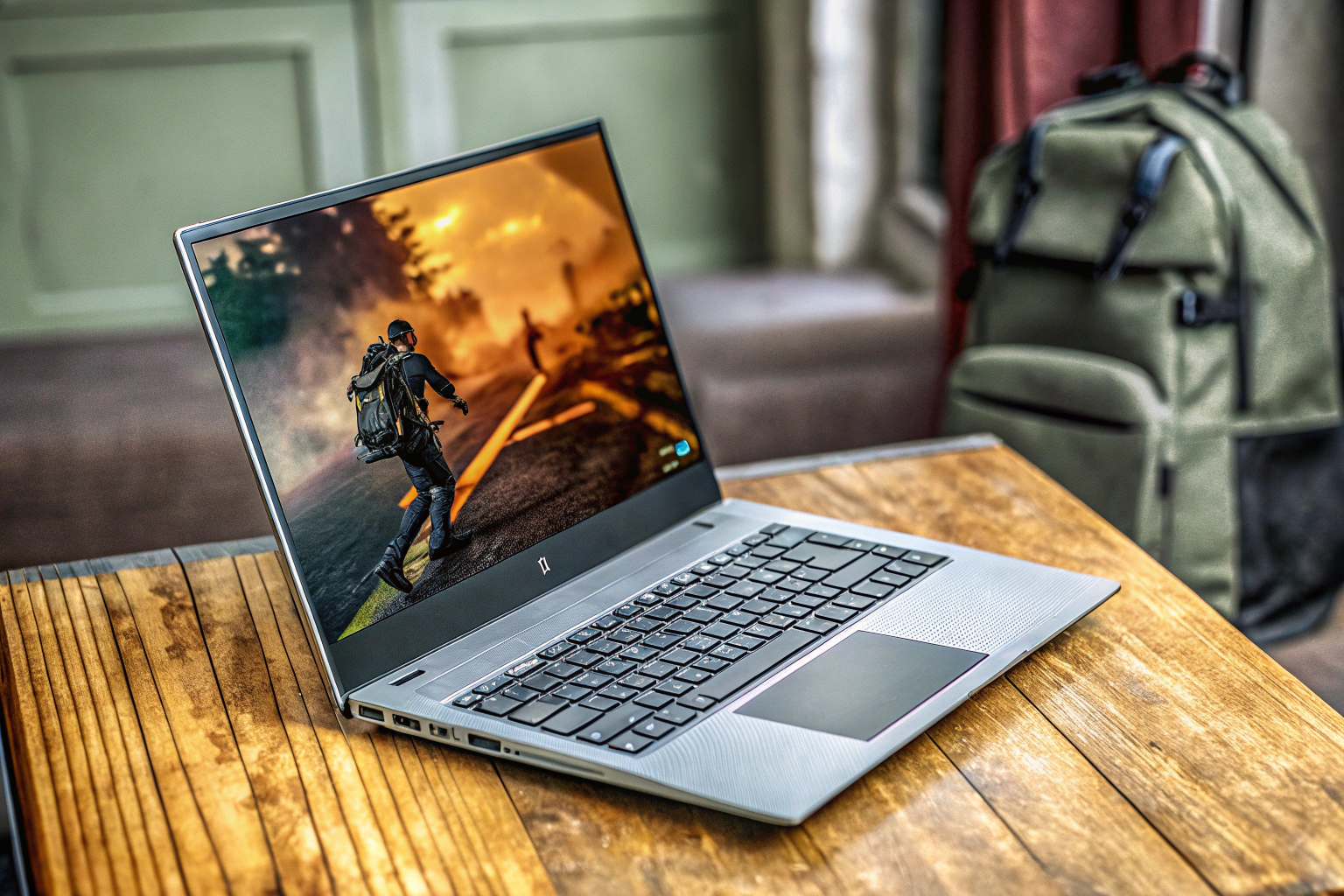 Ein Laptop zeigt ein beeindruckendes Spiel auf seinem Display, während im Hintergrund eine Reisetasche zu sehen ist. Laptop mit Spiel und Reisetasche